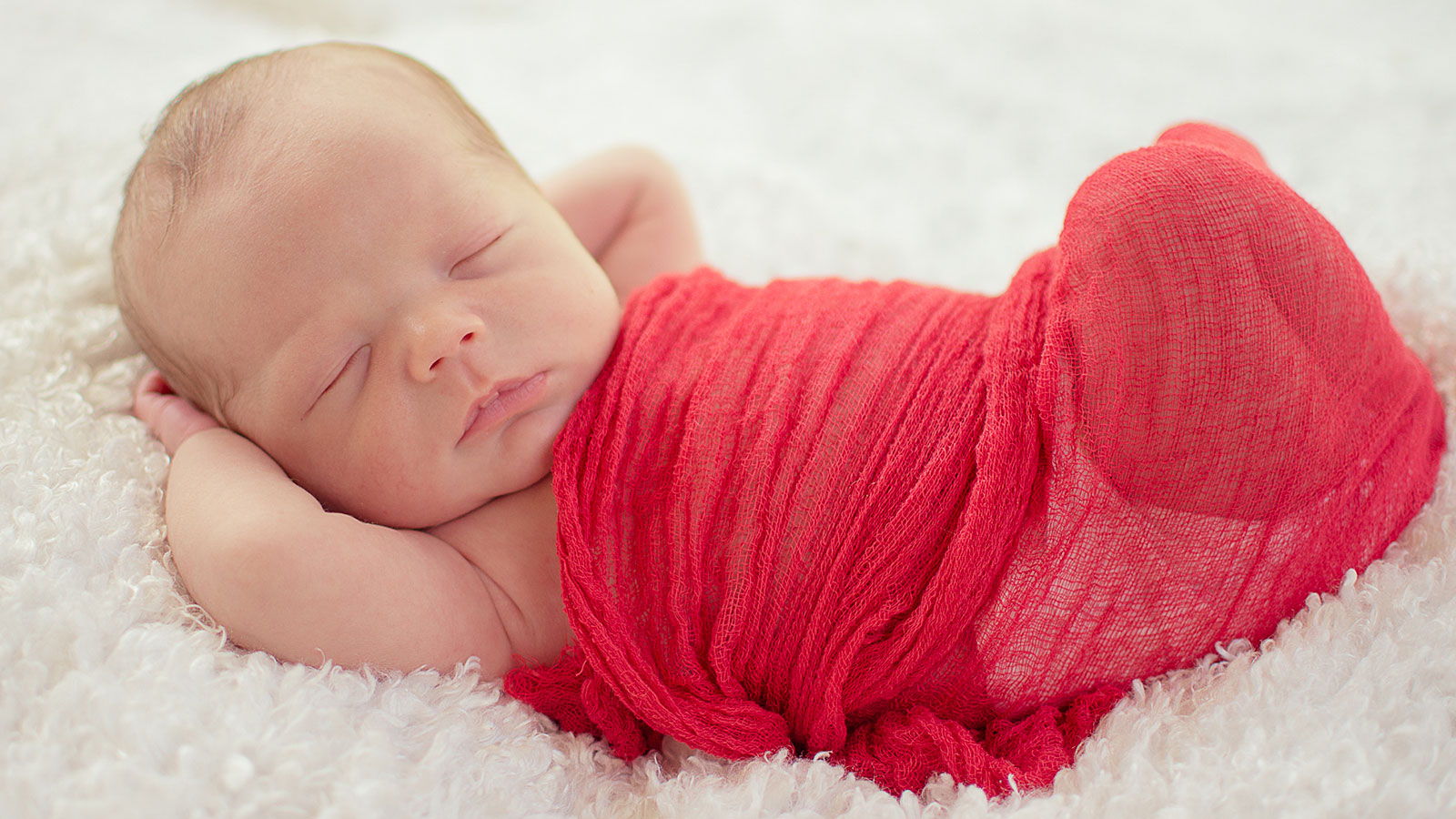 Portrait of newborn baby boy on white rug in red gauze swaddle by Needville, Texas family photographer Kristen Richards